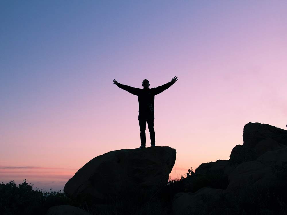 Gratitude , image of a man raising his two hands, standing on the large rock