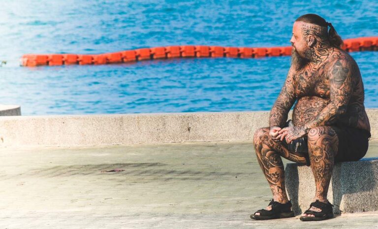 Unconditional happiness. image of man full of tattoos in his body sitting on cement beside ocean