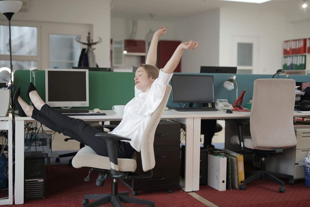Financial Happiness, a woman sitting in an office chair with hands up and foot under the table