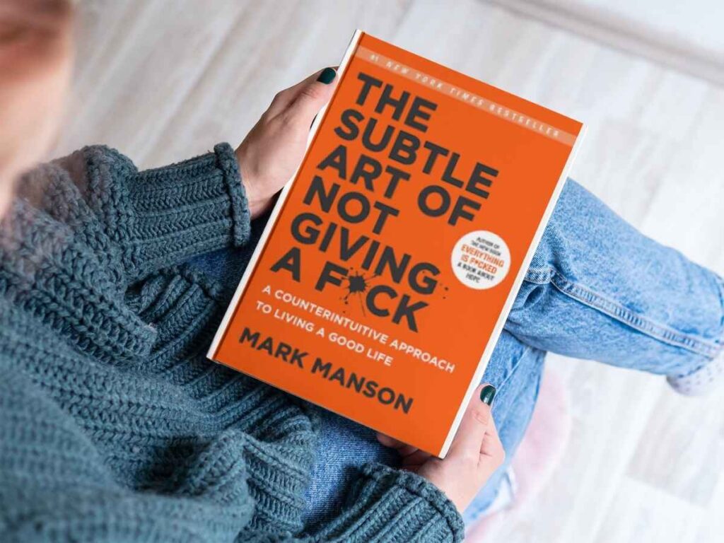 Holding a book of The Subtle Art of Not Giving a F*ck by Mark Manson